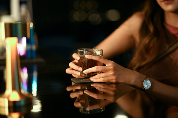 Close up shot young woman relaxing with glass of whiskey at bar counter