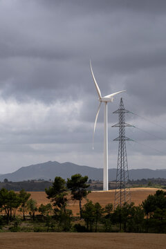 A wind turbine and a power line coexist in a field, with rolling hills in the distance, illustrating the balance between renewable energy and traditional power sources in serene rural settings in Ler