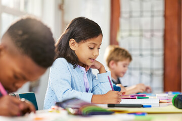 Cute little indian girl writing on her notebook at elementary school