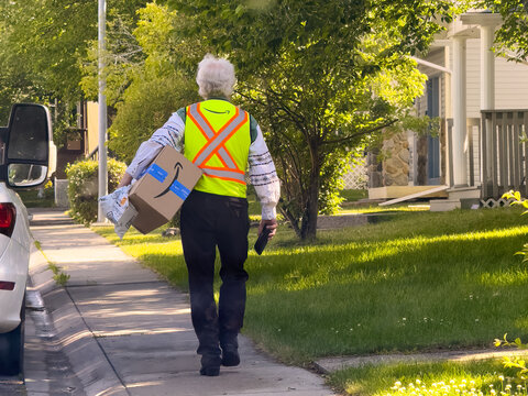 Calgary, Alberta, Canada. Jul 15, 2024. An Amazon delivery worker handling packages while delivering them in a neighborhood on a summer day.