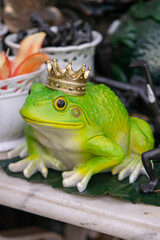 Green frog with a gold crown on a white ceramic figurine.