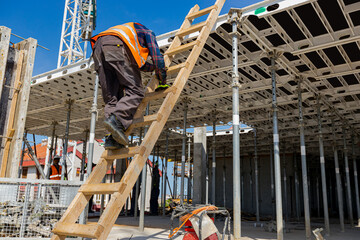 Rigger, worker is climbing on wooden ladder to the next floor made of demountable large mold.