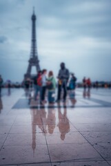 Obraz premium The Eiffel Tower is reflected in a wet Parisian square, blurred figures pass by.