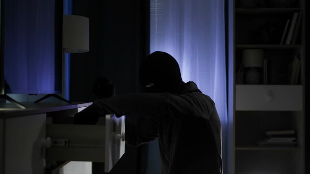 home security, male thief wearing balaclava and rummaging through things looking for valuable things and money in the room