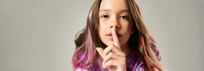 A stylish teenage girl with long hair holding her finger to her lips in a secretive gesture.