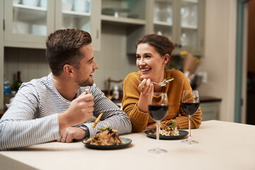 Happy, couple and eating food in home with wine on date night for romance in relationship with bonding. Man, woman and together with dinner or alcohol in kitchen with love, trust and soul connection.