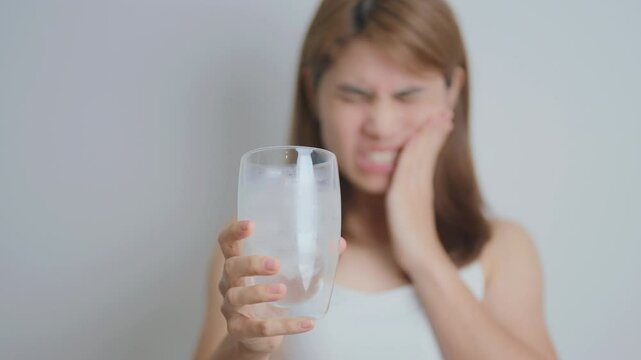 Teeth Sensitive to Cold concept. woman hold Ice Water glass and having toothache and pain after eat. Tooth Decay or Gum Disease, Grinding Teeth and Stress, Exposed Nerve Roots, Crack and Receding Gums