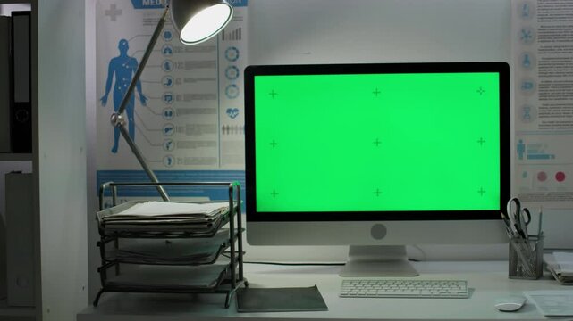 No people panning shot of modern computer monitor with blank green mockup screen with tracking markers on doctors desk in hospital, medical posters on wall