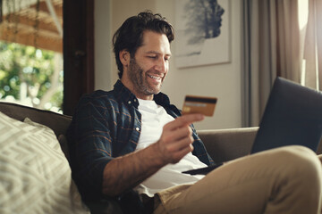 Man, home and smile on laptop with debit card on sofa for credit score, payment and saving plan. Rewards, happy and couch in living room for internet banking, budget and investment or finance