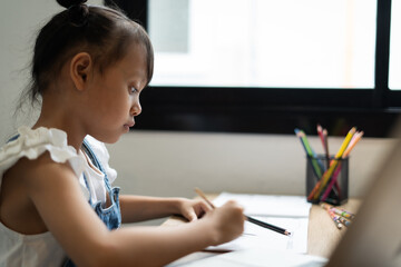 A young girl is sitting at a desk with a pencil and a piece of paper. She is focused on her work, possibly writing a story or a report