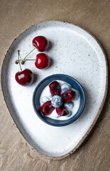 Fresh summer cherries with a dish of blueberries and yogurt on a teardrop shaped platter on a stone worktop
