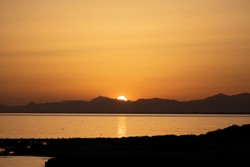 Horizontal photo of a sunset on the coast with the sun hiding behind the mountain.