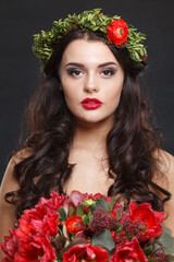 Naklejka premium Charming young woman with floral head wreath looking at camera while standing against black background