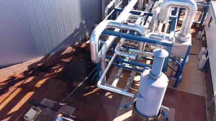 Drone shot moving up and over metal pipes and infrastructure at an industrial facility. This could be a water treatment plant, power plant, or desalination plant.