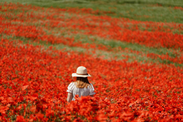Field poppies woman. Happy woman in a white dress and hat stand with her back a blooming field of poppy. Field of blooming poppies.