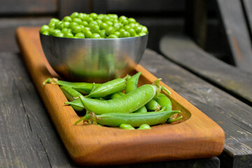 Fresh green pea pods onoak wood plate, pea in bowl on background