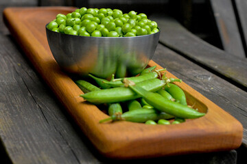 Fresh green pea pods on oak wood plate, pea in bowl on background