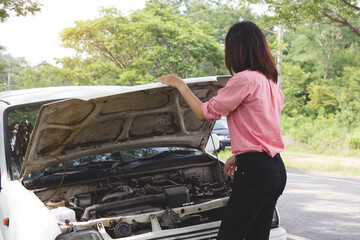 Women open hood of the vehicle and inspecting car engine for cause of breakdown on the roadside.