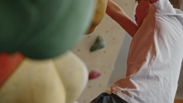 a 10-year-old boy in a white T-shirt during a climbing workout at an indoor climbing wall. An athlete is a climber in a difficult situation on a steep wall. Getting out of dangerous situations. 4k