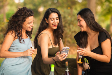 girlfriends laughing being happy at the park with a drink and phone 