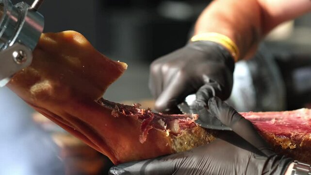 close up of hands man Chef cutting Extra quality dry-cured spanish ham Jamon very appetizing. detailed image of a ham cutter with knife cutting a thin slice of Iberico jamon. 4K.