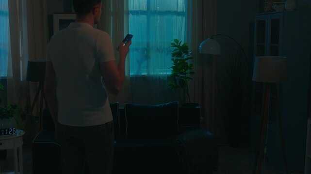 Smart home system dark room modern electronic house apartment Wi-Fi indoors night evening man guy male user homeowner householder use mobile phone turn lights on smartphone online control application