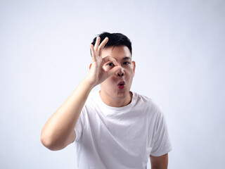 Fototapeta premium A young Asian man, wearing a white shirt and black watch, makes a playful expression while forming an 