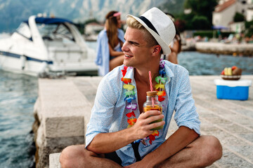 Happy young man enjoying a tropical cocktail on beach. Travel and summer vacation concept.