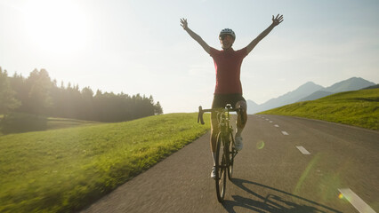 Happy female road racing cyclist in joy, with arms raised above her head, after successfully reaching a goal