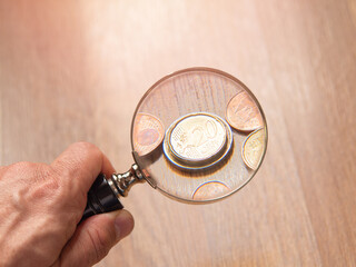 Hand Holding Magnifying Glass Over Coins