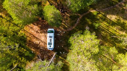 An aerial view of a campervan parked in a clearing within a dense Finnish forest. Sunlight dapples...