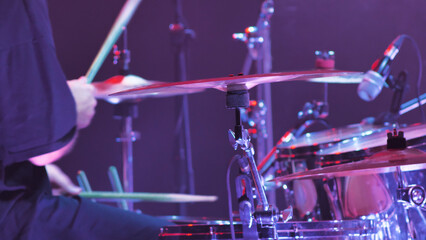 A musician passionately playing drums on a stage, bathed in vibrant lights during a live concert....