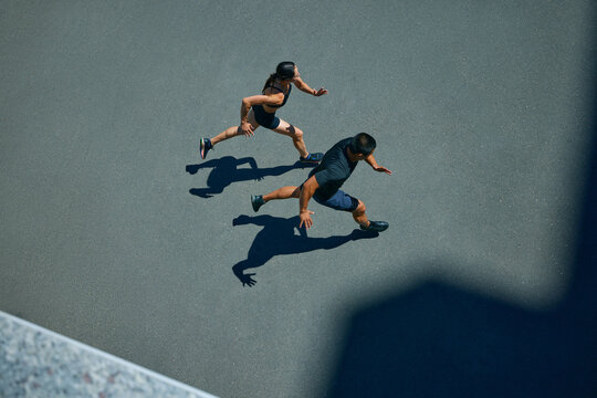 Young, athlete man and woman in sporty attire running together during pair workout on sunny summer day. Fit couple. Concept of sport and healthy lifestyle, pair training, leisure activity. - Powered by Adobe