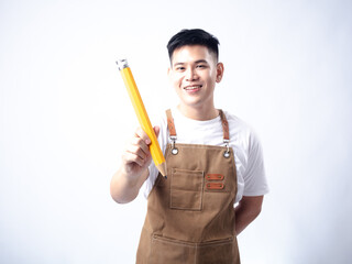 An Asian man in a white shirt and brown leather apron smiles while holding an oversized yellow pencil, standing against a light grey studio background