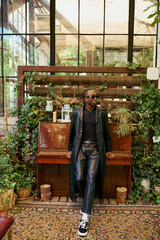 A dapper African American man, sitting on a bench in front of a piano in a vibrant garden.