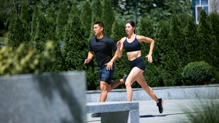 Athletic duo, one man and one woman, sprint together. Their high-energy run shows their fitness levels and commitment to staying in shape. Concept of sport, pair training, leisure activity.
