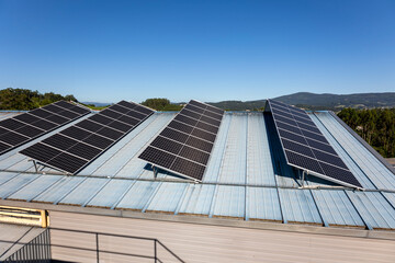 Fototapeta premium This image portrays several solar panels installed on the blue metal roof of a building, set against a clear, blue sky and distant hills in the background, emphasizing renewable energy.