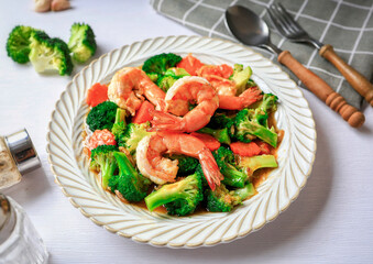 Stir fried broccoli with shrimp in a white ceramic plate witn spoon and fork on white table background