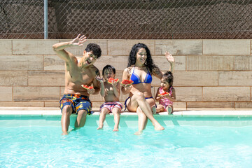 Family enjoying watermelon by the pool, smiling and waving while sitting on the edge.