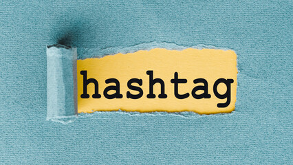 A close-up image of the word hashtag written in black text on a torn piece of yellow paper,...