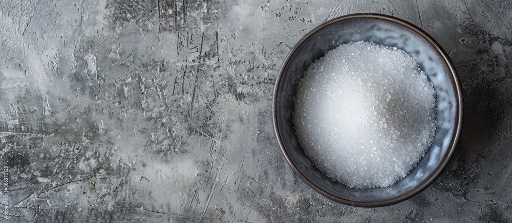 Poster Top view of a bowl with granulated sugar on a textured grey table providing ample space for text in the image