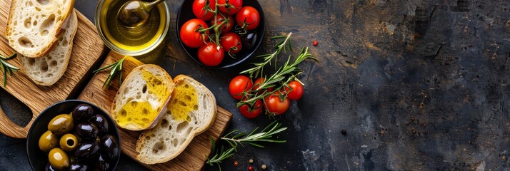 Top-down view of a rustic Mediterranean spread featuring sliced bread, olives, cherry tomatoes, olive oil, and sprigs of rosemary on a textured dark background