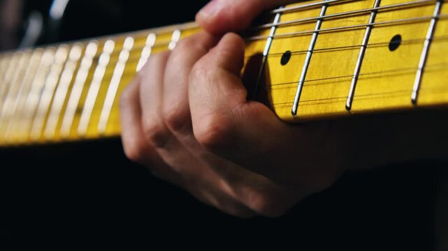 Close-up of a man playing a guitar, with emphasis on his fingers pressing the strings and fret to the guitar's fingerboard. Guitarist playing rhythm honing his skills in a garage