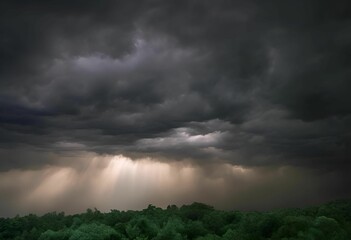 Dramatic dark storm clouds with sun rays breaking through over a lush green forest
