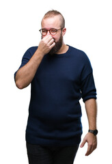 Young caucasian hipster man wearing sunglasses over isolated background smelling something stinky and disgusting, intolerable smell, holding breath with fingers on nose. Bad smells concept.