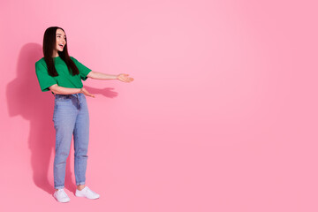 Full length photo of cheerful pretty lady dressed green t-shirt showing arms looking empty space isolated pink color background