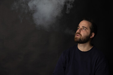 Young man exhaling smoke on black background