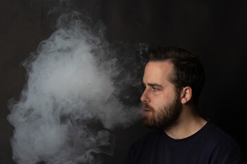 Young man exhaling smoke on black background