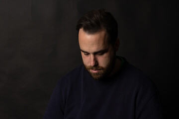 Bearded man looking down with sad expression on black background