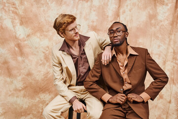 Two handsome multicultural men in elegant attire sitting closely together.